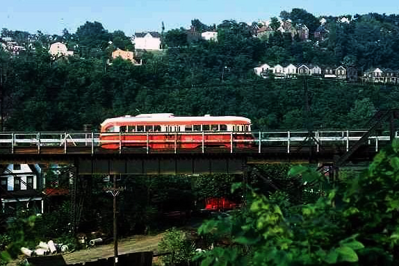 Orange and cream colored trolley train with homes and trees in the background.