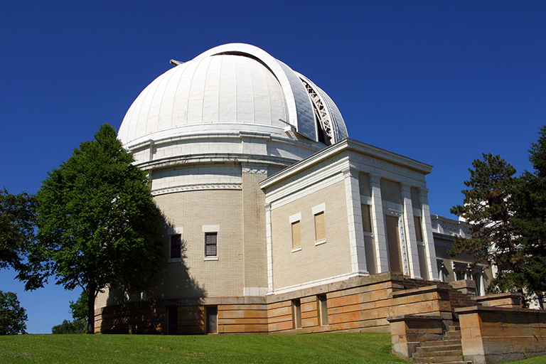 White and beige dome-shaped observatory building with trees and blue sky.