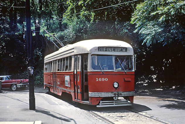 Orange and cream colored trolley train with classic red car in background.